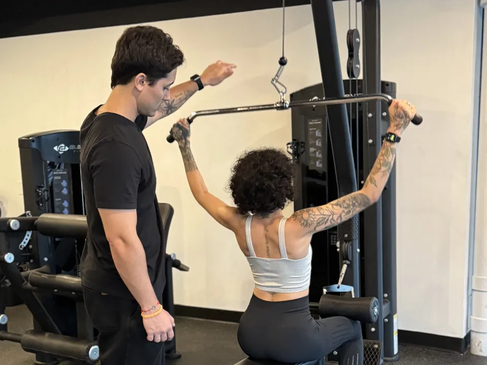 Guilherme guiding a client through a lat pulldown with proper technique